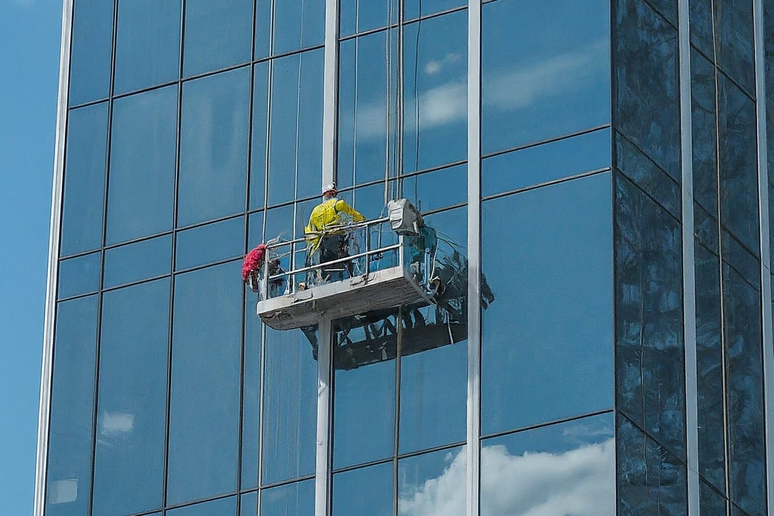 A man cleaning the windows of a high-rise building using a safety harness and squeegee.